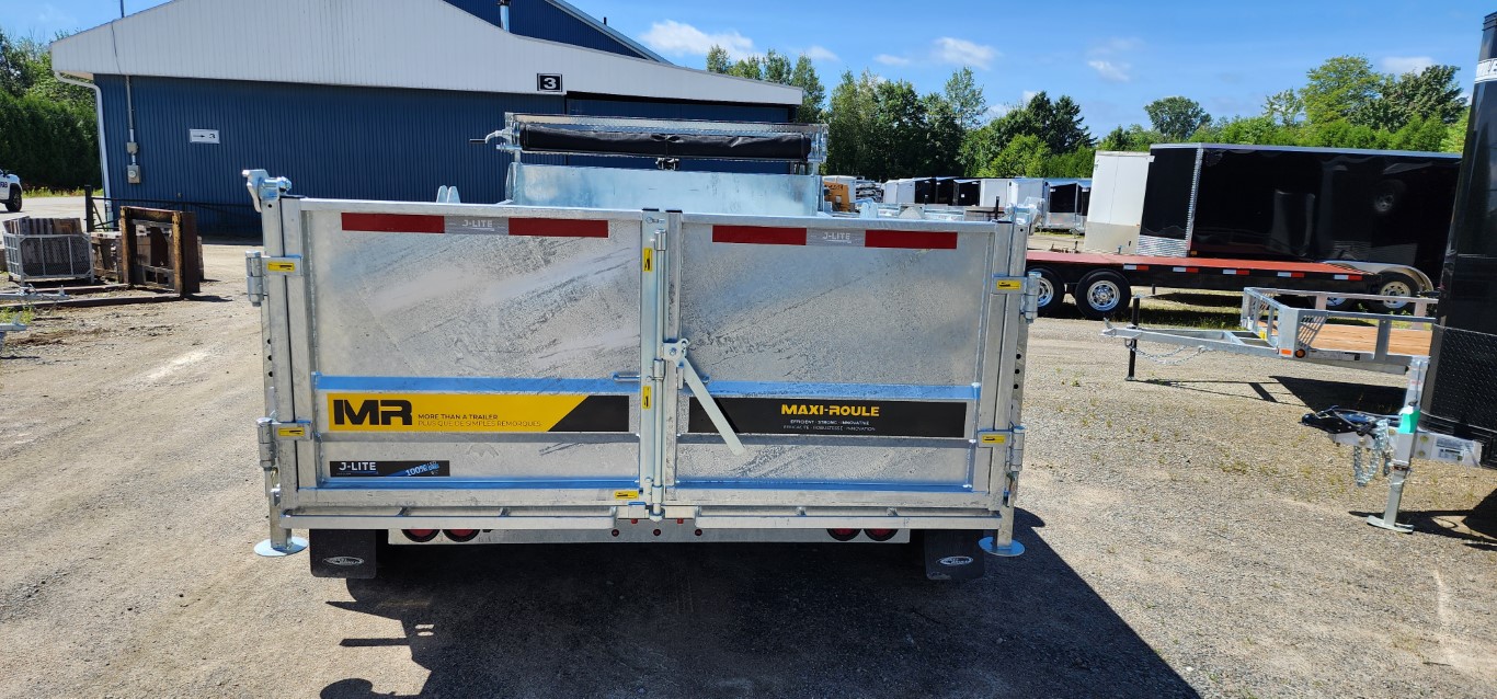 Une remorque à benne basculante est garée sur un terrain en gravier devant un bâtiment.