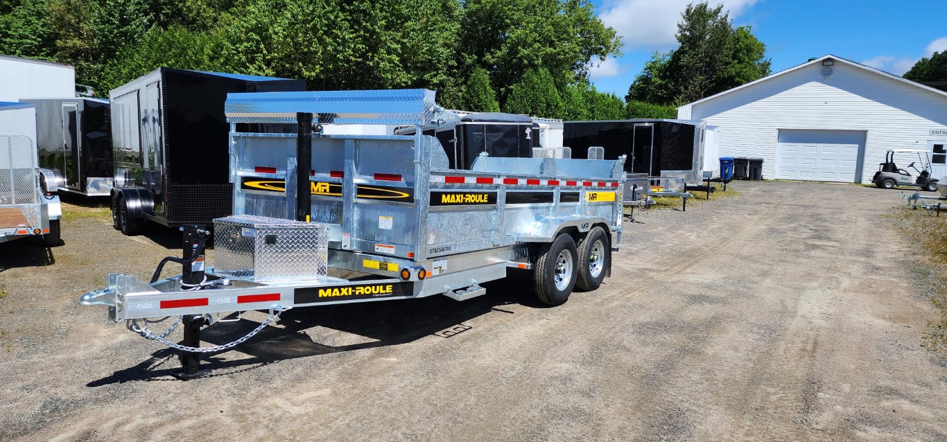 Une remorque est garée sur un terrain en terre devant un bâtiment.