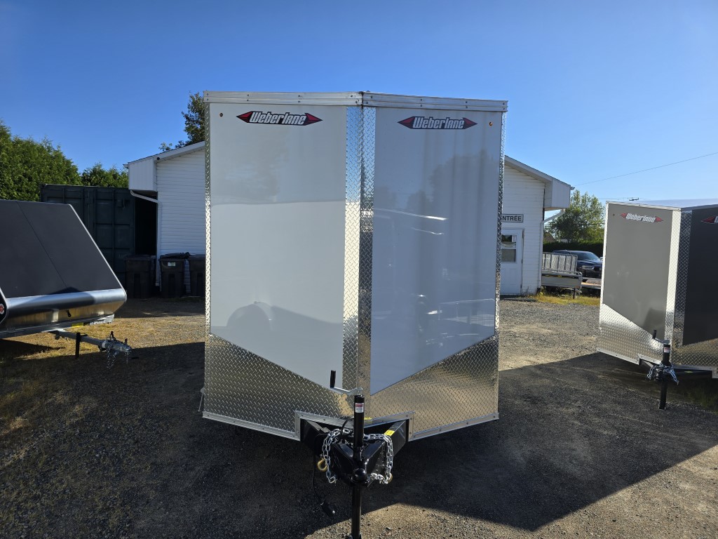 Une remorque blanche est garée devant un garage.