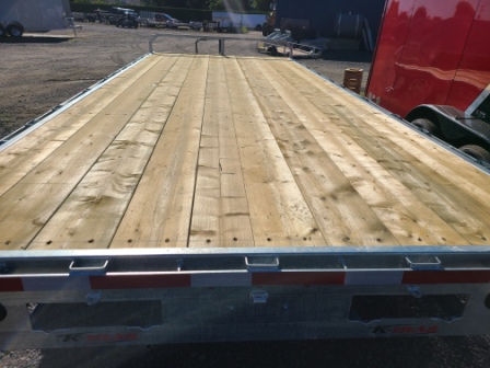 Une remorque à plateau avec un pont en bois est garée sur un parking