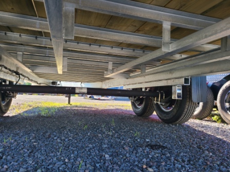 Une remorque avec un pont en bois est garée sur du gravier.