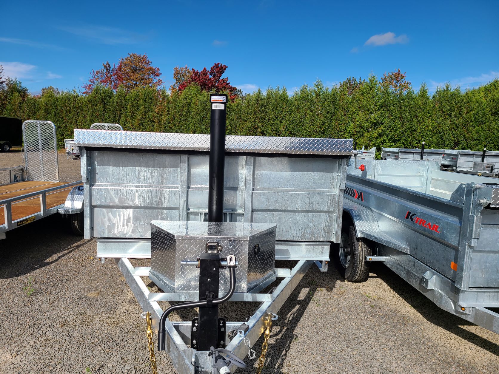 Une remorque avec une benne à ordures attachée est garée dans un terrain en gravier.